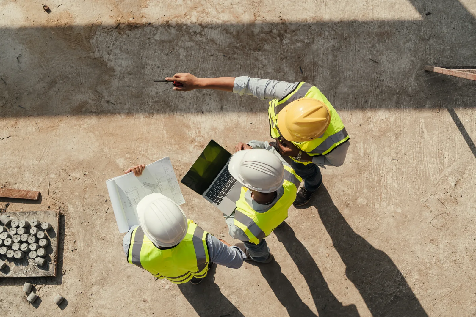 Overhead view of a project team reviewing drawings and a laptop on a construction site